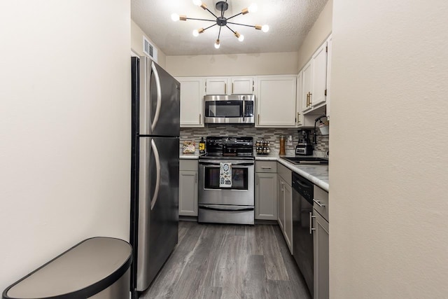 kitchen featuring an inviting chandelier, dark wood-style flooring, decorative backsplash, light countertops, and appliances with stainless steel finishes