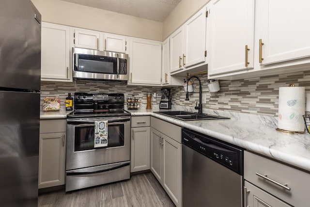 kitchen featuring light wood-style floors, stainless steel appliances, decorative backsplash, and a sink