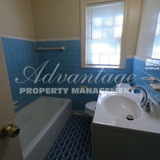 bathroom featuring toilet, tile walls, wainscoting, tile patterned floors, and vanity