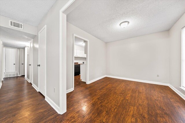 empty room with a textured ceiling, dark wood-type flooring, and baseboards