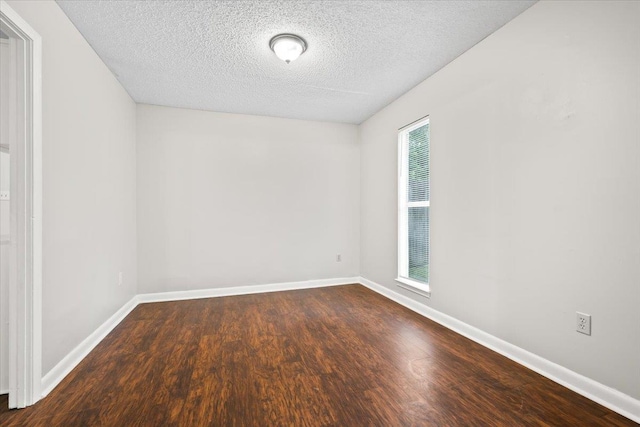 spare room with dark wood-type flooring, a textured ceiling, and baseboards