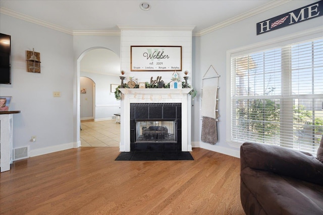 living area with arched walkways, ornamental molding, wood finished floors, a tile fireplace, and baseboards