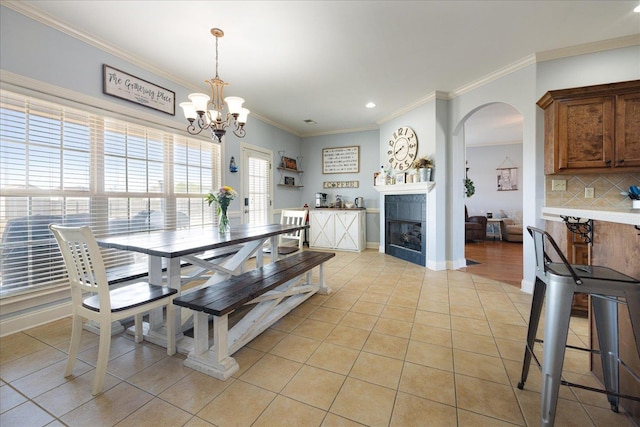dining area with light tile patterned floors, a chandelier, ornamental molding, arched walkways, and a fireplace