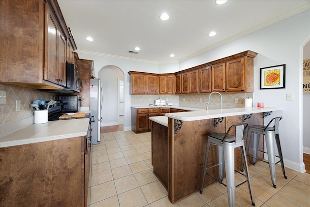 kitchen with arched walkways, a peninsula, a breakfast bar, light tile patterned flooring, and tasteful backsplash
