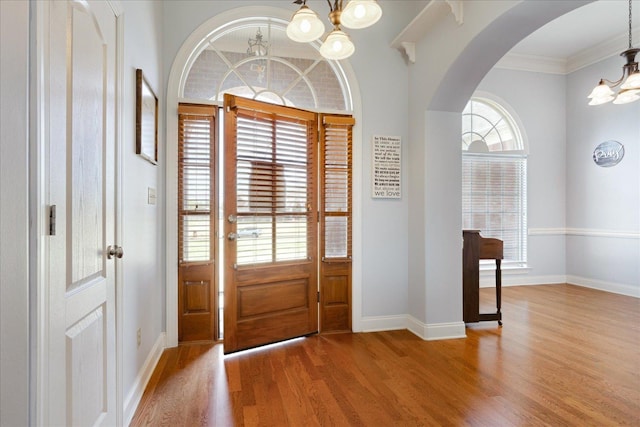 entrance foyer featuring a chandelier, arched walkways, light wood-style floors, baseboards, and ornamental molding