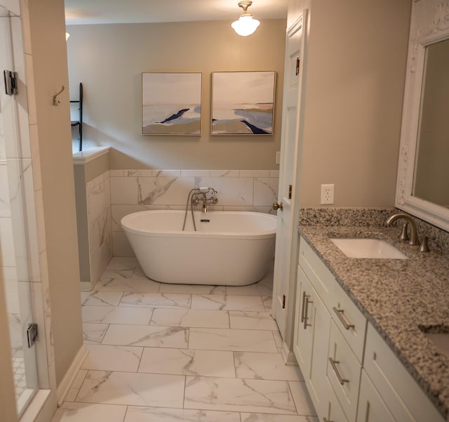 full bath featuring marble finish floors, a freestanding tub, double vanity, and a wainscoted wall