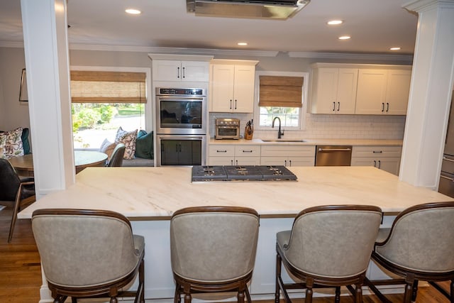 kitchen with a sink, appliances with stainless steel finishes, crown molding, white cabinets, and backsplash