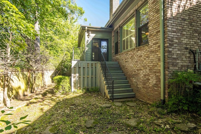 view of side of home featuring brick siding, a chimney, and fence