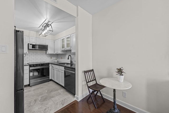 kitchen featuring stainless steel appliances, a sink, dark countertops, and white cabinetry