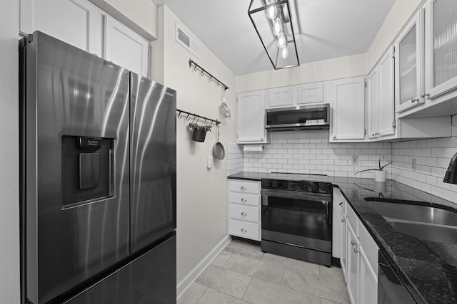 kitchen featuring stainless steel appliances, baseboards, dark stone counters, decorative backsplash, and white cabinets