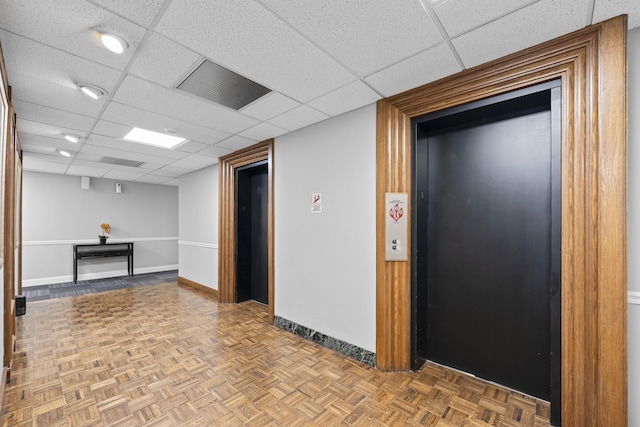 spare room with elevator, a drop ceiling, and baseboards