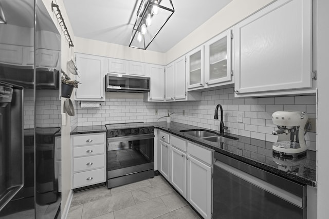 kitchen with appliances with stainless steel finishes, a sink, decorative backsplash, dark stone counters, and white cabinetry