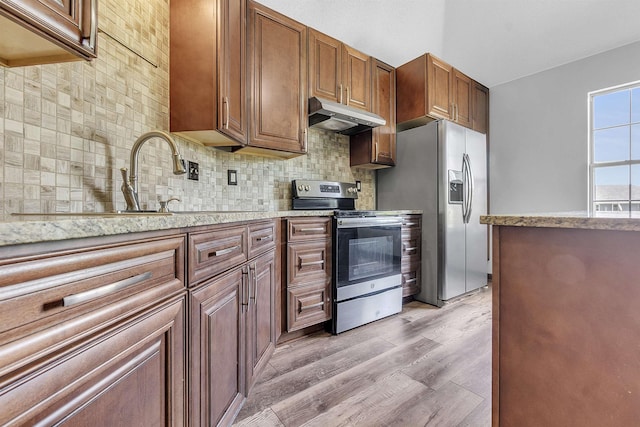 kitchen with stainless steel appliances, under cabinet range hood, decorative backsplash, light wood-style floors, and light stone countertops