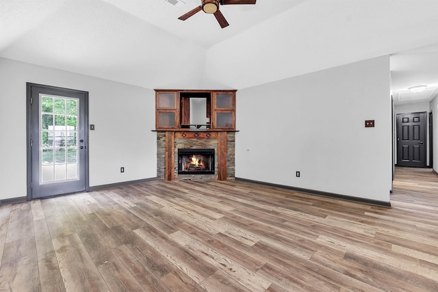 unfurnished living room with a ceiling fan, light wood finished floors, lofted ceiling, a warm lit fireplace, and baseboards
