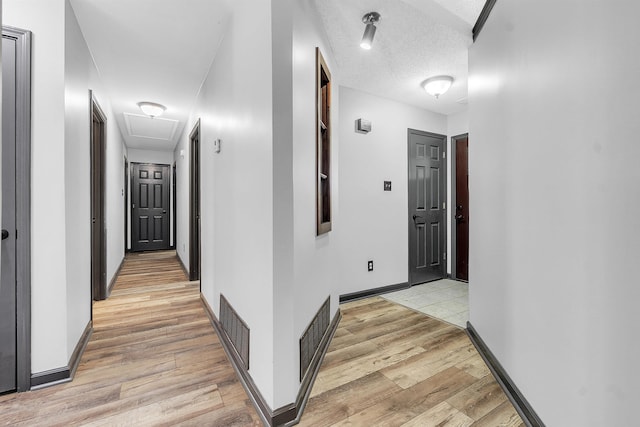 corridor featuring attic access, light wood-style floors, and baseboards