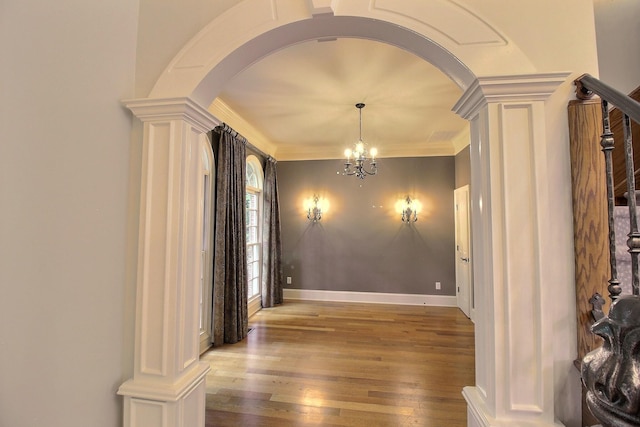 unfurnished dining area with arched walkways, decorative columns, wood finished floors, a chandelier, and crown molding