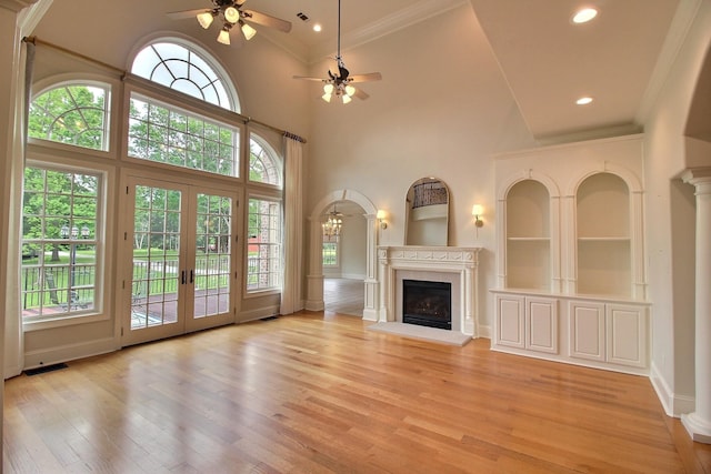 unfurnished living room featuring a ceiling fan, a high end fireplace, ornamental molding, light wood-style flooring, and high vaulted ceiling