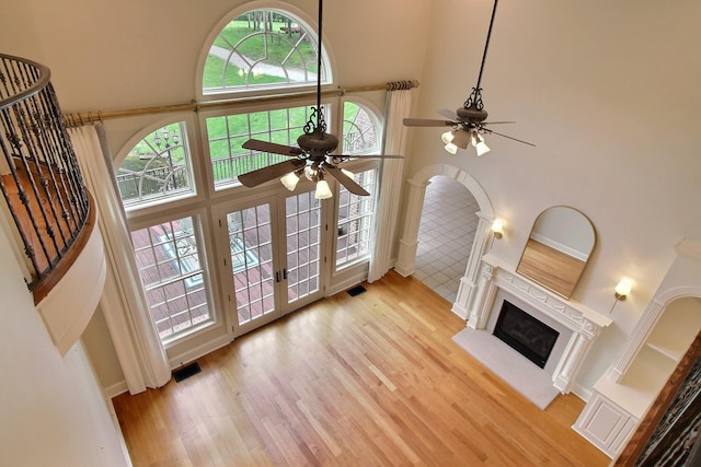 unfurnished living room featuring a high ceiling, a ceiling fan, wood finished floors, a glass covered fireplace, and french doors