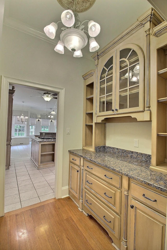 kitchen with open shelves, crown molding, glass insert cabinets, a chandelier, and dark stone counters