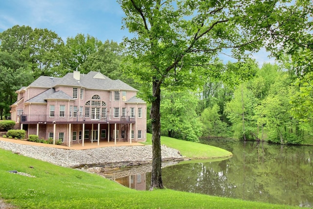rear view of property with a deck with water view, a yard, a chimney, brick siding, and a patio