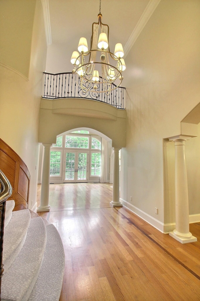 entryway featuring ornate columns, ornamental molding, wood finished floors, a chandelier, and a towering ceiling