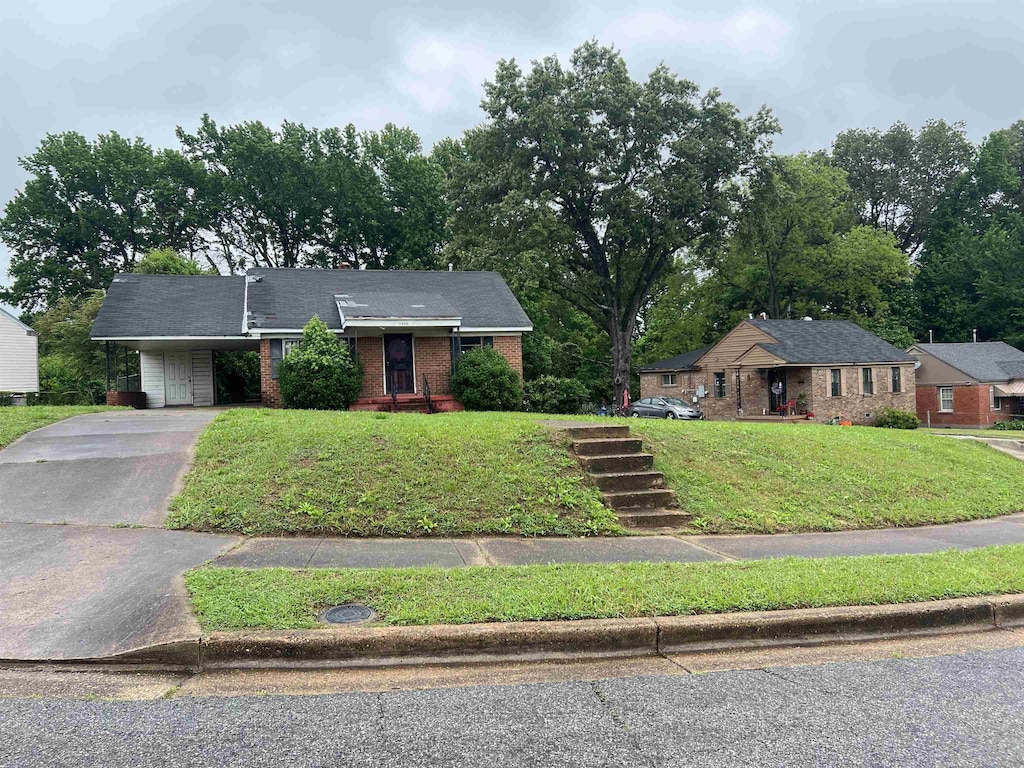 ranch-style house featuring brick siding, asphalt driveway, a carport, and a front yard
