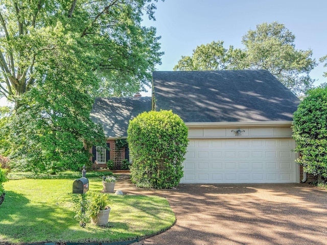 view of property hidden behind natural elements featuring roof with shingles, an attached garage, driveway, and a front yard