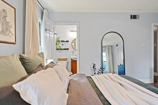 bedroom with ensuite bathroom, wood finished floors, and baseboards