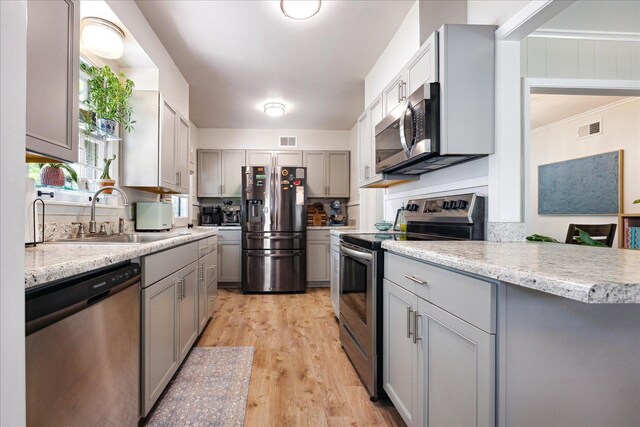 kitchen with stainless steel appliances, a sink, gray cabinetry, light wood-style flooring, and ornamental molding