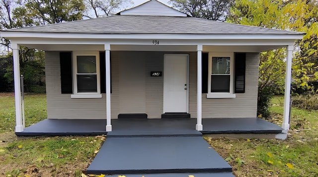 view of front of house featuring covered porch, a shingled roof, and a front lawn