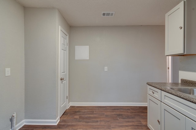 kitchen featuring dark wood-style flooring, dark countertops, baseboards, and white cabinetry