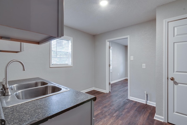 kitchen featuring a sink, dark wood-type flooring, dark countertops, a textured ceiling, and baseboards