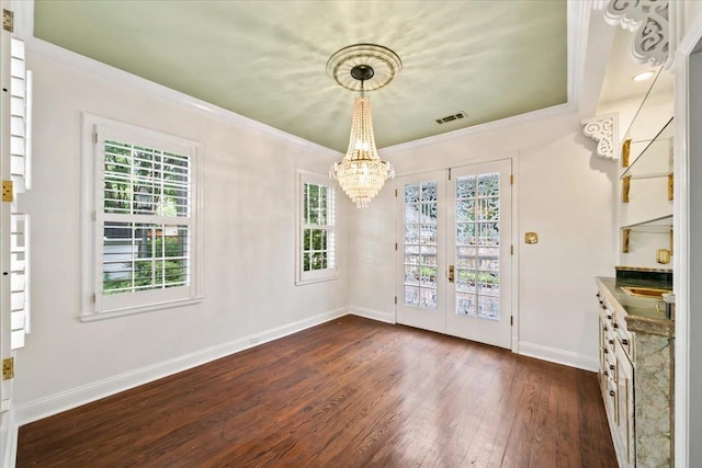 unfurnished dining area featuring dark wood finished floors, baseboards, a chandelier, crown molding, and french doors