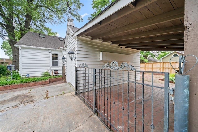 view of side of property with a patio, fence, roof with shingles, a chimney, and driveway