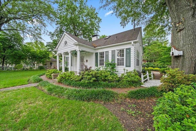 rear view of property featuring a lawn, a chimney, a porch, and a shingled roof