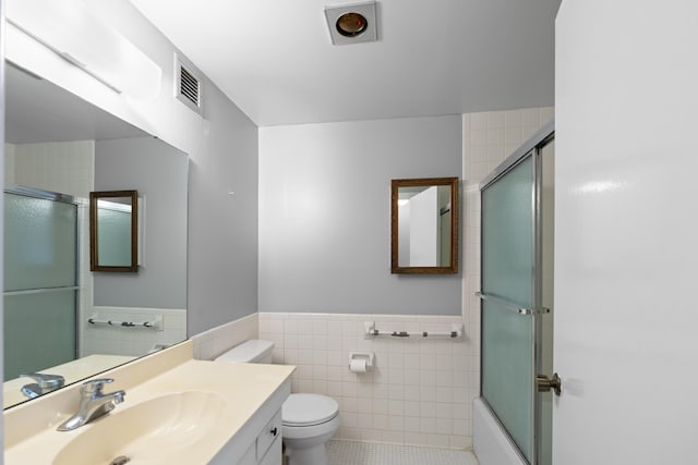 full bath with tile walls, toilet, a wainscoted wall, shower / bath combination with glass door, and vanity