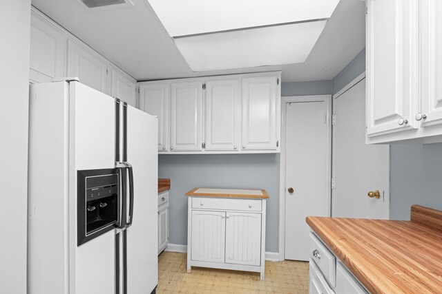kitchen with white refrigerator with ice dispenser, wood counters, white cabinetry, light floors, and baseboards