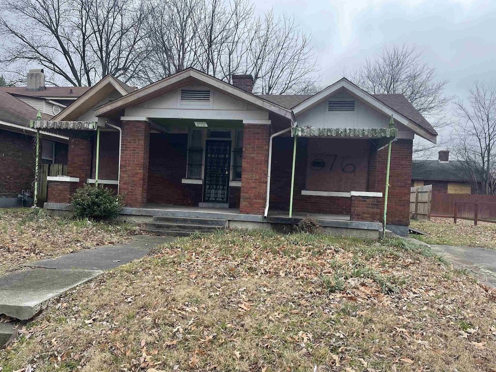 view of front of home featuring covered porch, brick siding, a chimney, and fence