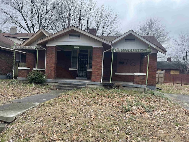 view of front of home featuring covered porch, brick siding, a chimney, and fence