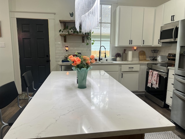 kitchen with stainless steel appliances, a sink, tasteful backsplash, white cabinetry, and a center island
