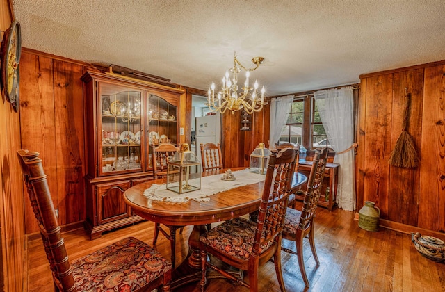 dining space with wooden walls, a textured ceiling, a chandelier, and hardwood / wood-style flooring