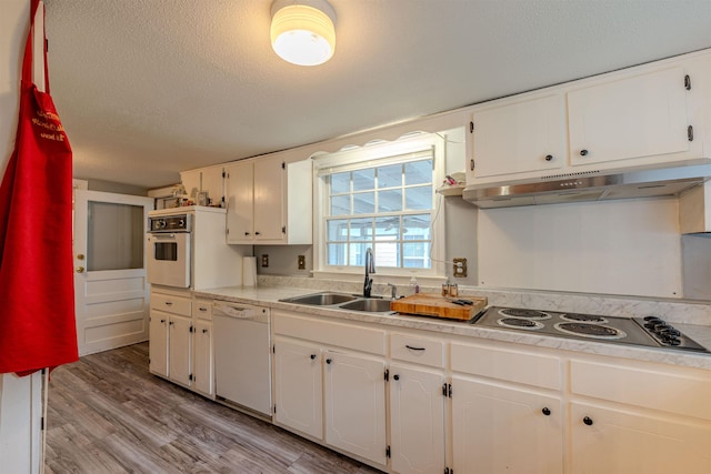 kitchen with white appliances, under cabinet range hood, a sink, white cabinets, and a textured ceiling