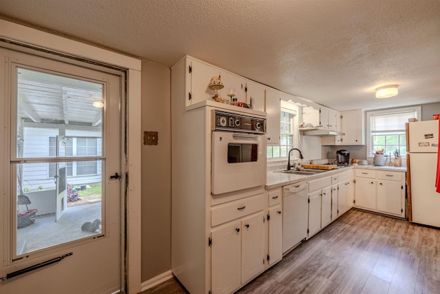 kitchen featuring white appliances, a sink, light wood-type flooring, a textured ceiling, and white cabinetry