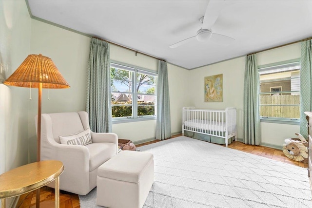 bedroom featuring a nursery area, ceiling fan, and wood finished floors