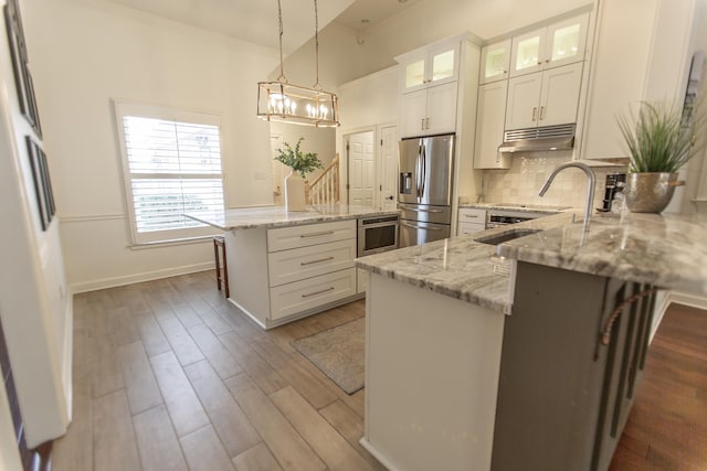 kitchen with stainless steel appliances, wood finished floors, tasteful backsplash, light stone countertops, and crown molding
