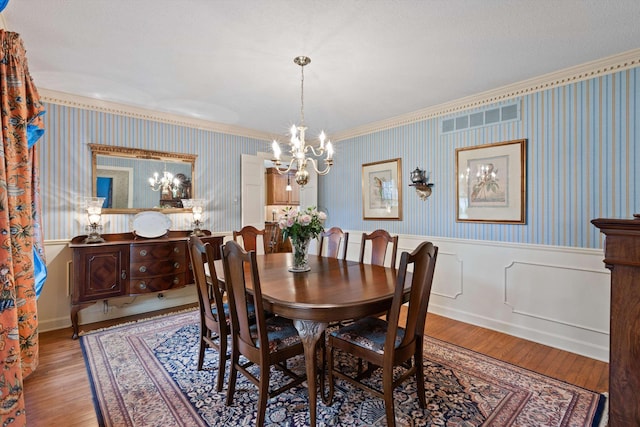 dining area featuring a chandelier, crown molding, wainscoting, wallpapered walls, and wood finished floors