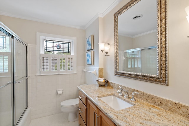 full bathroom featuring toilet, vanity, ornamental molding, tile walls, and a wainscoted wall