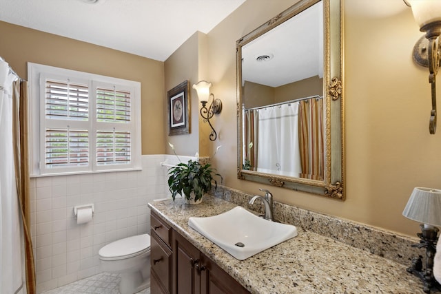 full bath with tile patterned floors, tile walls, toilet, vanity, and a wainscoted wall