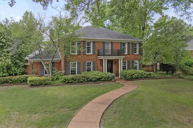 georgian-style home with brick siding, a front yard, and a balcony