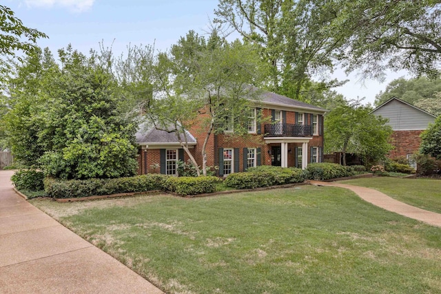 colonial house featuring brick siding, a front yard, and a balcony